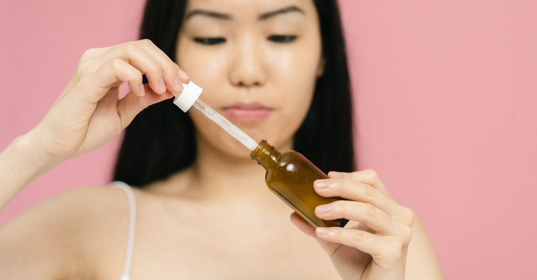 Glass anti-aging serum bottle with dropper on a white marble surface, representing a luxury anti-aging serum for 30s skincare routine.